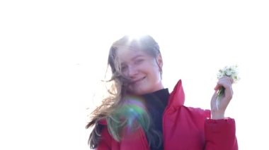 Çiçek tutan ve bahar çiçeklerine gülümseyen bir kız.