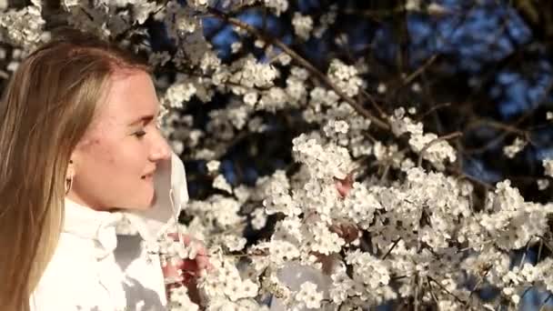 Ξανθιά κοπέλα με λευκή μάσκα βγάζει σέλφι σε φόντο ανθισμένων οπωροφόρων δέντρων. — Αρχείο Βίντεο