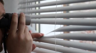 Adam insanları gözetliyor, dürbünü gözlem için kullanıyor.