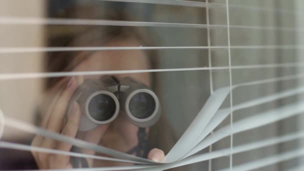 Girl in binoculars looking through blinds from his window — Video Stock