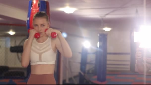 Nainen nyrkkeilijä harjoittelee ennen taistelua, tyttö tutkii taistelulakkoja. — kuvapankkivideo