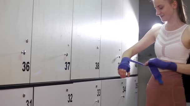 Girl boxer preparing for a workout in the gym, she rolls bandages on her hands. — ストック動画