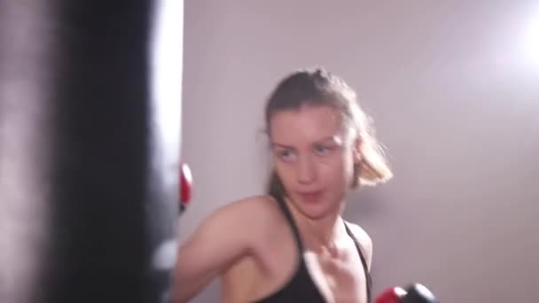 Uma jovem forte treina no salão de boxe. A menina bate um saco de perfuração. — Vídeo de Stock