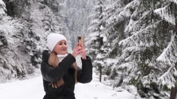 Meisje fotografeert een prachtig winterbos, wandelt en kijkt naar de besneeuwde natuur in januari — Stockvideo