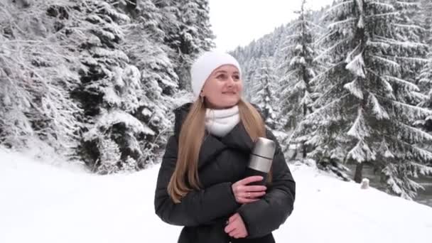 Κορίτσι κρατώντας ένα θερμός του καφέ στα χέρια της και περπατώντας σε ένα χιονισμένο δρόμο στη μέση του δάσους — Αρχείο Βίντεο