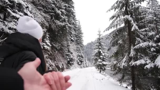 Een paar verliefde wandelingen op een winterweg, ze houden elkaars hand vast, een prachtig besneeuwd bos — Stockvideo