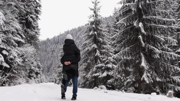 Liefdevol koppel op de weg in het midden van het winterbos, man tilt zijn vrouw in zijn armen — Stockvideo