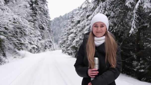 Het meisje houdt de sneeuw in haar handen en blaast het op, ze heeft plezier in het winterbos. — Stockvideo