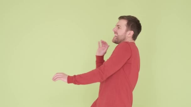 Cheerful smiling young man in orange sweater funny dancing on yellow and green background — Stockvideo