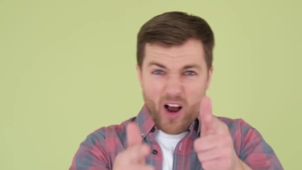 An adult man having fun on a yellow-green background in the studio, he pretends to shoot — Vídeo de Stock