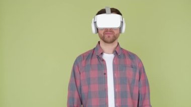 Genç bir adam yenilikçi modellik için VR gözlükleri kullanıyor. Stüdyoda sarı ve yeşil arka planda 3D gözlüklü bir adam var..