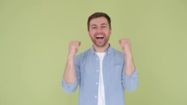 Handsome young man rejoices, raising his arms, feeling victory, close up, on green background