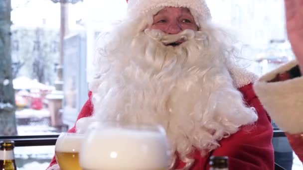 Mikulás nagy fehér szakállal beszél a barátaival egy kávézóban, kezében egy pohár sör. — Stock videók