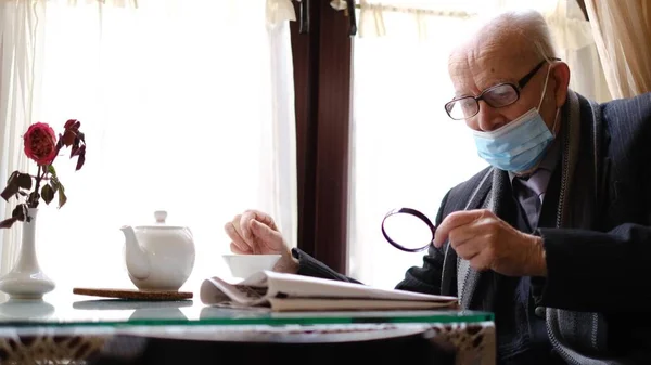 Avô de cabelos grisalhos está sentado em um café bebendo chá, ele está lendo um jornal. — Fotografia de Stock