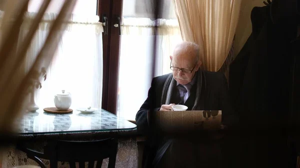 Velho avô lê a imprensa enquanto está sentado em um café. O pensionista está descansando — Fotografia de Stock