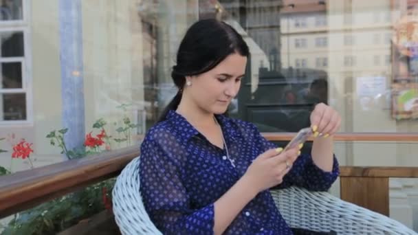 Aluna alegre jovem ruiva, com seu sorriso fofo localização no interior do café moderno, usando telefone celular, verificando newsfeed em suas contas de rede social. Menina bonita surfando a internet no celular — Vídeo de Stock