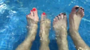 Happy group of young friends hanging out and chatting at the side of the pool in the summertime. legs in the pool