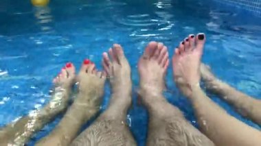 Happy group of young friends hanging out and chatting at the side of the pool in the summertime. legs in the pool