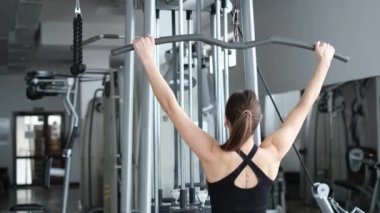 Jimnastik salonundaki kadın, sırt egzersizi yapıyor. Atletik kız aşağı çekiyor..