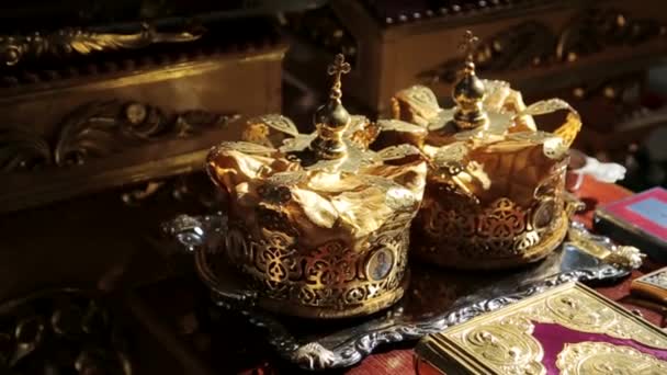 Coroa de ouro com pedras preciosas no guardanapo vermelho no altar na igreja. cerimónia de casamento tradicional, espaço para texto. religião — Vídeo de Stock