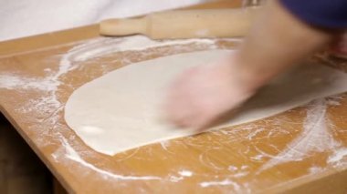 Kadın ahşap bir masada hamur yoğuruyor.