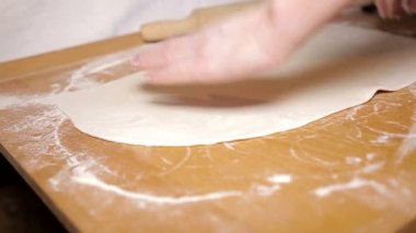 Kadın ahşap bir masada hamur yoğuruyor.