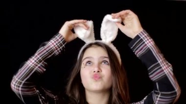 Portrait of a happy little girl with bunny ears looking up at copyspace isolated on a black background