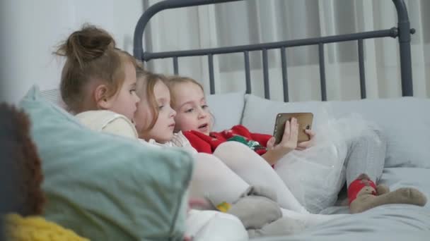 Children of a group of girls playing on the Internet from a mobile smartphone on the couch, happy family — Wideo stockowe