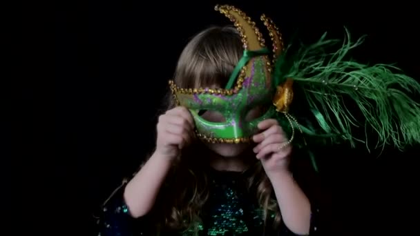 Niña en una máscara de carnaval verde, mirando a la cámara, bebé feliz — Vídeos de Stock