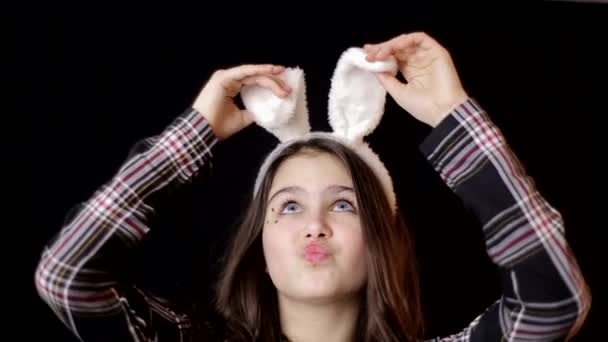 Portrait of a happy little girl with bunny ears looking up at copyspace isolated on a black background — Stockvideo