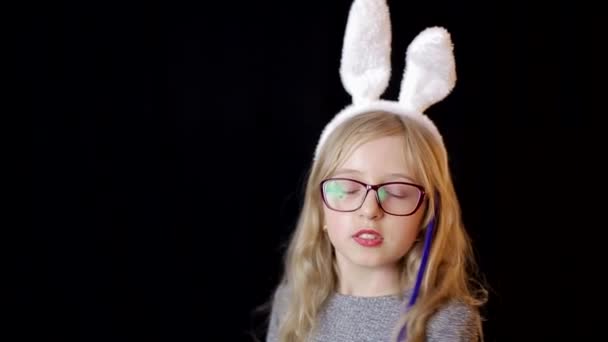 漂亮的少女，带着复活节兔子的耳朵，手里拿着棒棒糖。乡村木制背景. — 图库视频影像