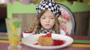 Tatlı küçük kız pasta yiyor. Pasta ve çilekli küçük güzel kız. Çocuk tatlı yiyor. Kız masada kaşıkla yemek yiyor.