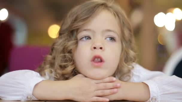 A beautiful little girl with light hair, looking into the camera with a gentle smile, treating the school photo shoot. — Stockvideo