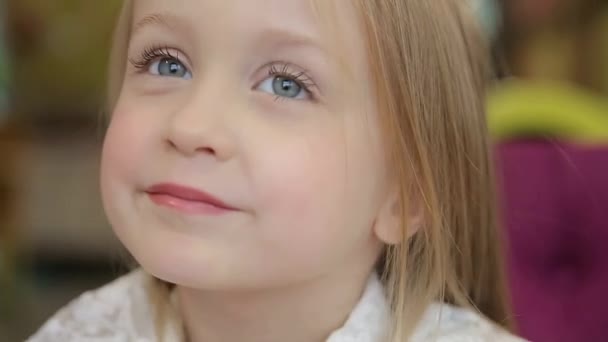 A beautiful little girl with light hair, looking into the camera with a gentle smile, treating the school photo shoot. — Stock video