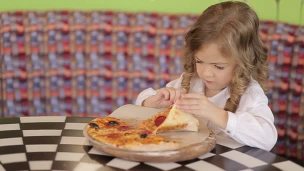 Nice little European baby eating pizza. A hungry child who takes a bite from pizza on a pizza. — Vídeo de stock