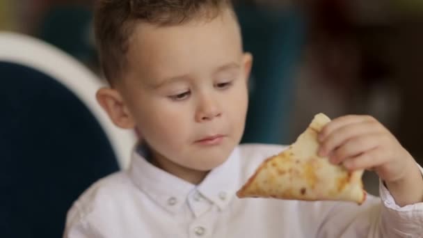 Маленький мальчик на кухне ест маленькую пиццу, очень охотно — стоковое видео