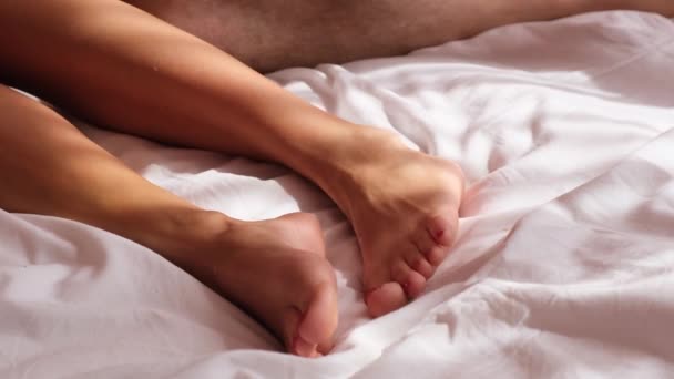 Κοντινό πλάνο των ποδιών ανδρών και γυναικών που αναπαύονται στο κρεβάτι. Ζευγάρι ερωτευμένο το πρωί κάτω από μια ζεστή κουβέρτα — Αρχείο Βίντεο