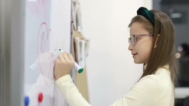 Ένα κοριτσάκι ζωγραφίζει ένα μαρκαδόρο σε έναν πίνακα στο σχολείο. Έξυπνο παιδί. — Αρχείο Βίντεο