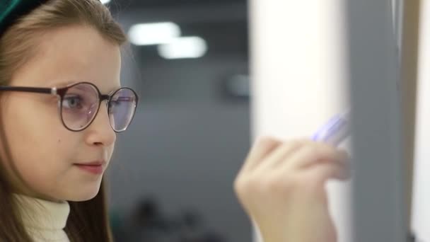 Gadis kecil menarik spidol di papan tulis di sekolah. Anak pintar berkacamata untuk meningkatkan penglihatan. — Stok Video