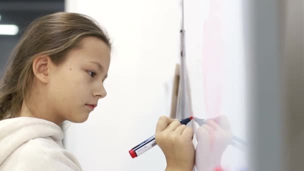 Liten skolflicka flicka skriver en markör på svarta tavlan i skolan. — Stockvideo