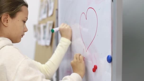 Pequeña colegiala escribe un marcador en la pizarra en la escuela. — Vídeo de stock