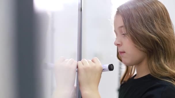 Una pequeña adolescente va a la escuela, dibuja con un marcador en la pizarra — Vídeos de Stock