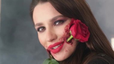 Ağzında kırmızı bir gül tutan bir kızın portresi. Cadılar Bayramı için makyaj, ağzında gül çiçeği.