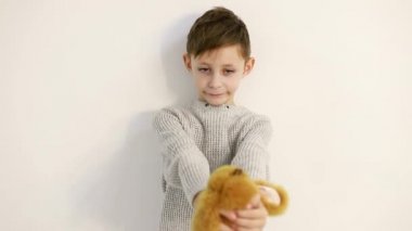 Beyaz arka planda yumuşak bir oyuncağı olan küçük çocuk nazikçe oyuncağa sarılıyor.