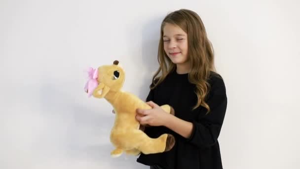 Una niña con un juguete suave sobre un fondo blanco, abraza tiernamente el juguete. — Vídeo de stock