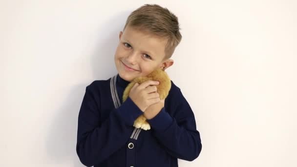 Vacker liten pojke med en mjuk leksak på en vit bakgrund, ömt kramar leksaken — Stockvideo