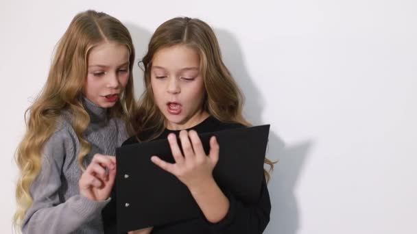 Två vackra små systrar tittar på surfplattan, smarta barn med smart teknik. — Stockvideo
