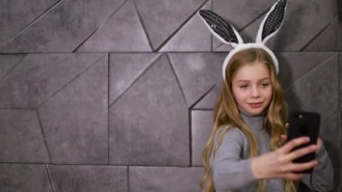 Genç kız elinde akıllı bir telefonla eğleniyor. Tavşan kulağı takıyor.