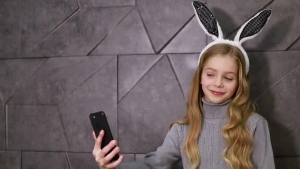 스마트폰으로 즐겁게 놀고 있는 10 대 소녀가 토끼 귀를 하고 있습니다. — 비디오