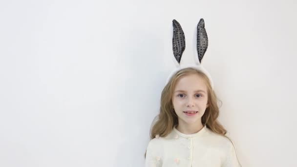 Lächelndes kleines Mädchen im Mantel, gekleidet in die Ohren eines Osterhasen, ein glückliches Kind wartet auf die Feiertage — Stockvideo